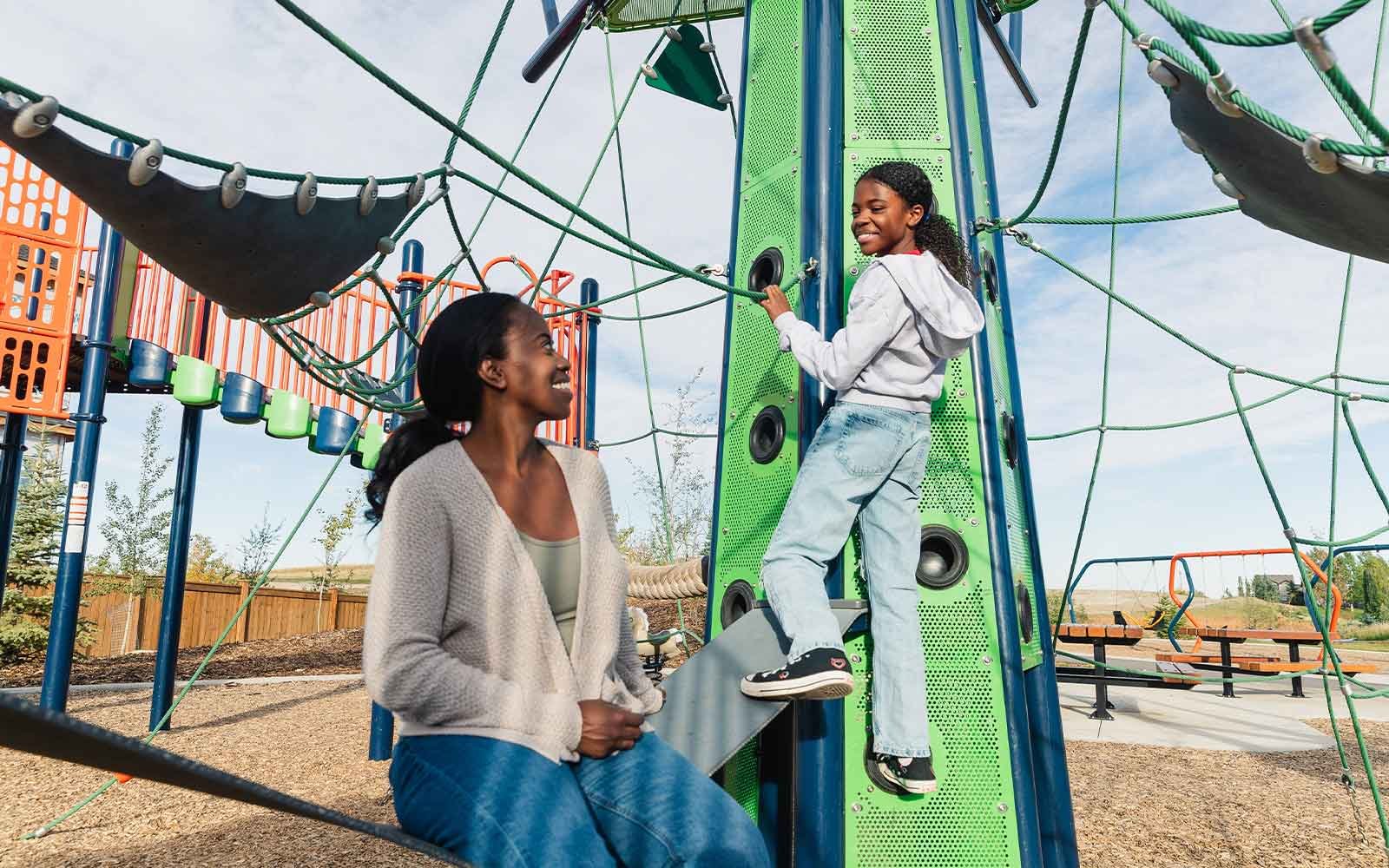 A child plays at the playground while her mother looks on