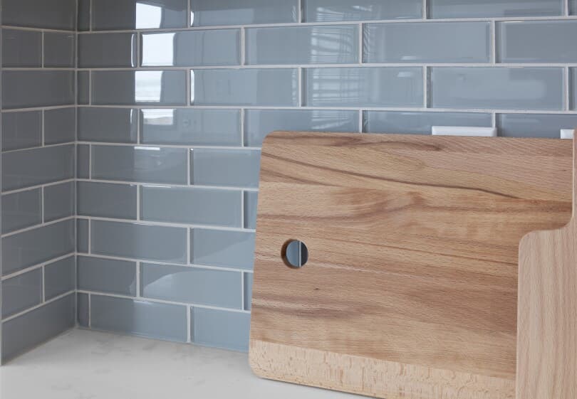 Close up view of grey blue subway tile on kitchen backsplash with a cutting board on a white quartz countertop