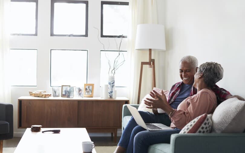 Older couple laughing while sitting on a couch looking at a laptop