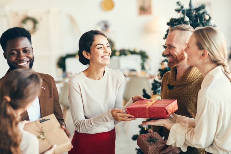 Group of elegant young people exchanging gifts and smiling cheerfully during Christmas party