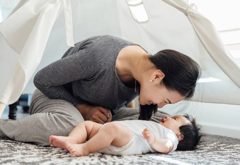 Mother smiling and leaning over her baby lying on the floor