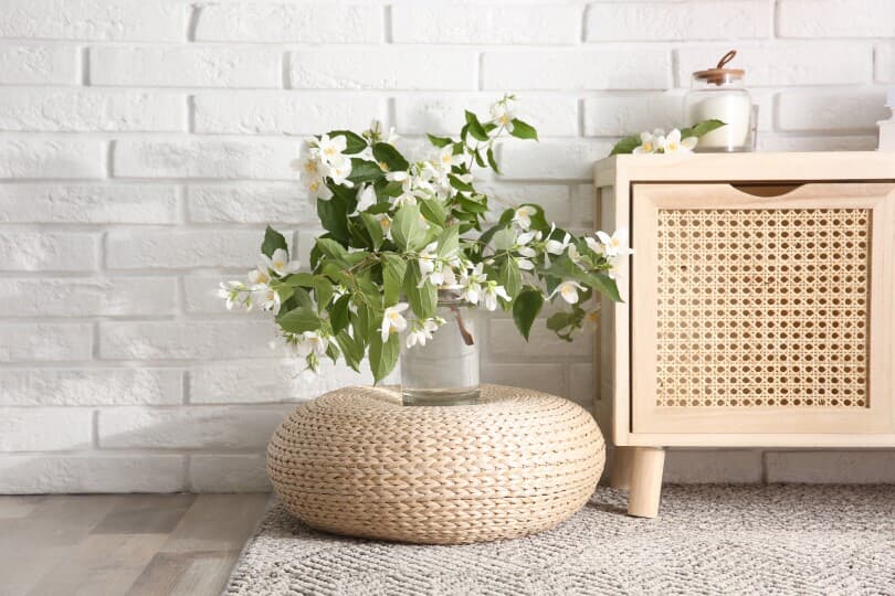 Jasmine flowers in glass vase near white brick wall indoors