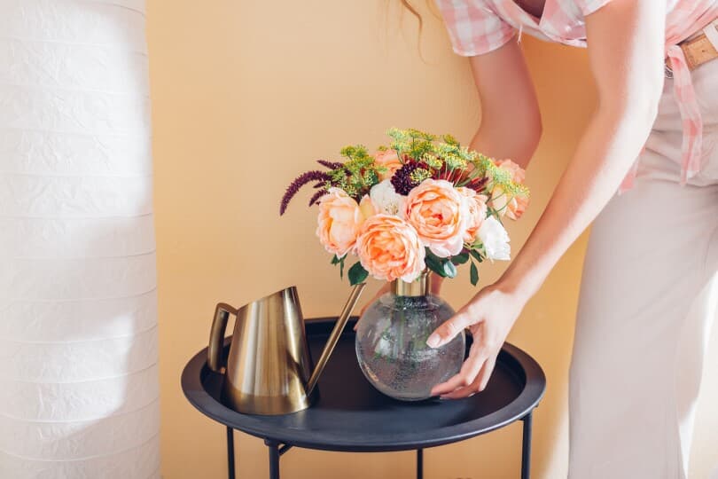 Woman puts vase with bouquet of flowers on table at home