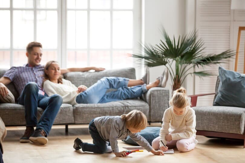 Couple relaxing on a couch while kids color in a book on the floor - 810x540
