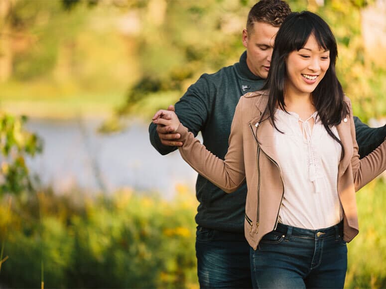 A couple walks across a log near the Bow River in Seton Ridge.