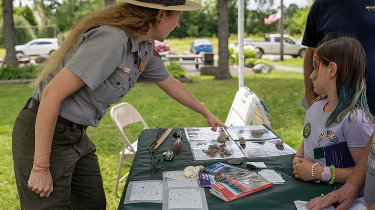A ranger points at a photo of an animal on the Katahdin Woods and Waters table at Patten Pioneer Day. Credit NPS/Gin Majka