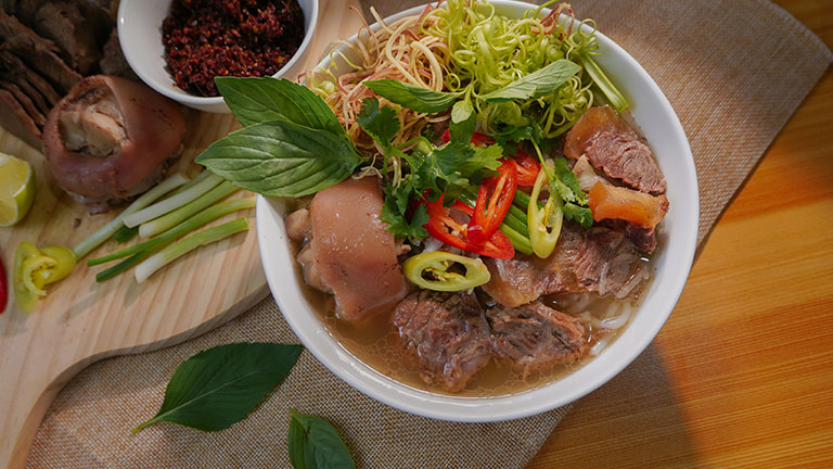 A bowl of traditional Vietnamese pho topped with fresh herbs, sliced peppers, and tender beef.