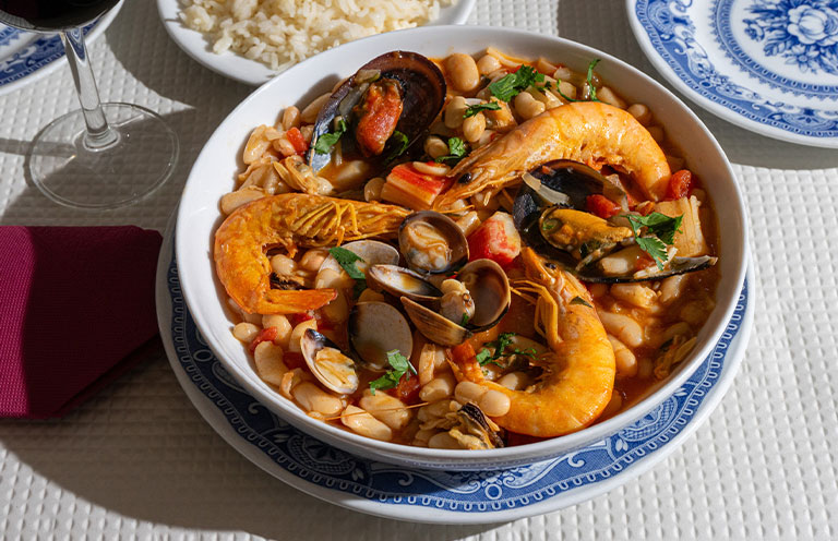 A traditional Alentejo restaurant serves a vibrant seafood feijoada. This dish features prawns, shellfish, and beans in a rustic clay pot, offering a hearty and authentic Portuguese experience.