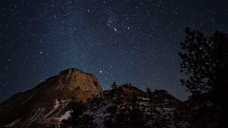 Clusters of bright white stars over sandstone cliffs in the night sky.