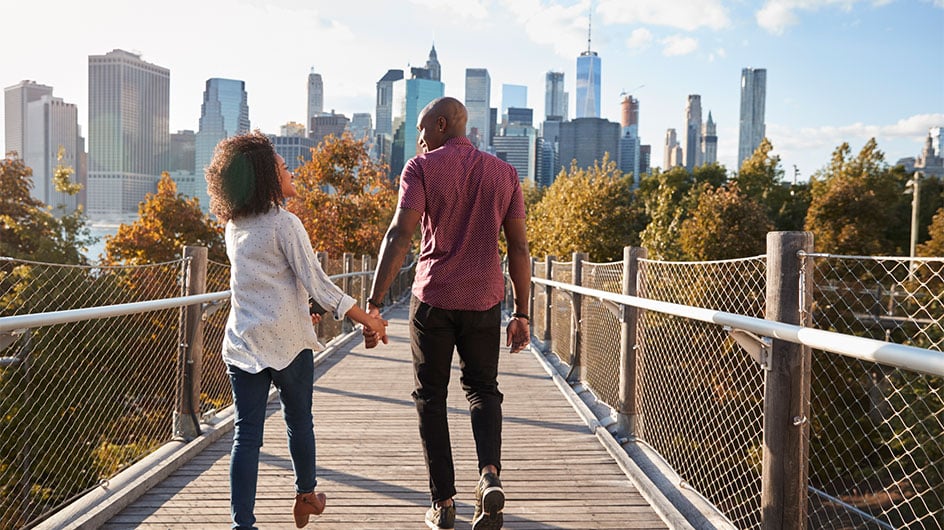 man and woman holding hand walking towards New York City skyline