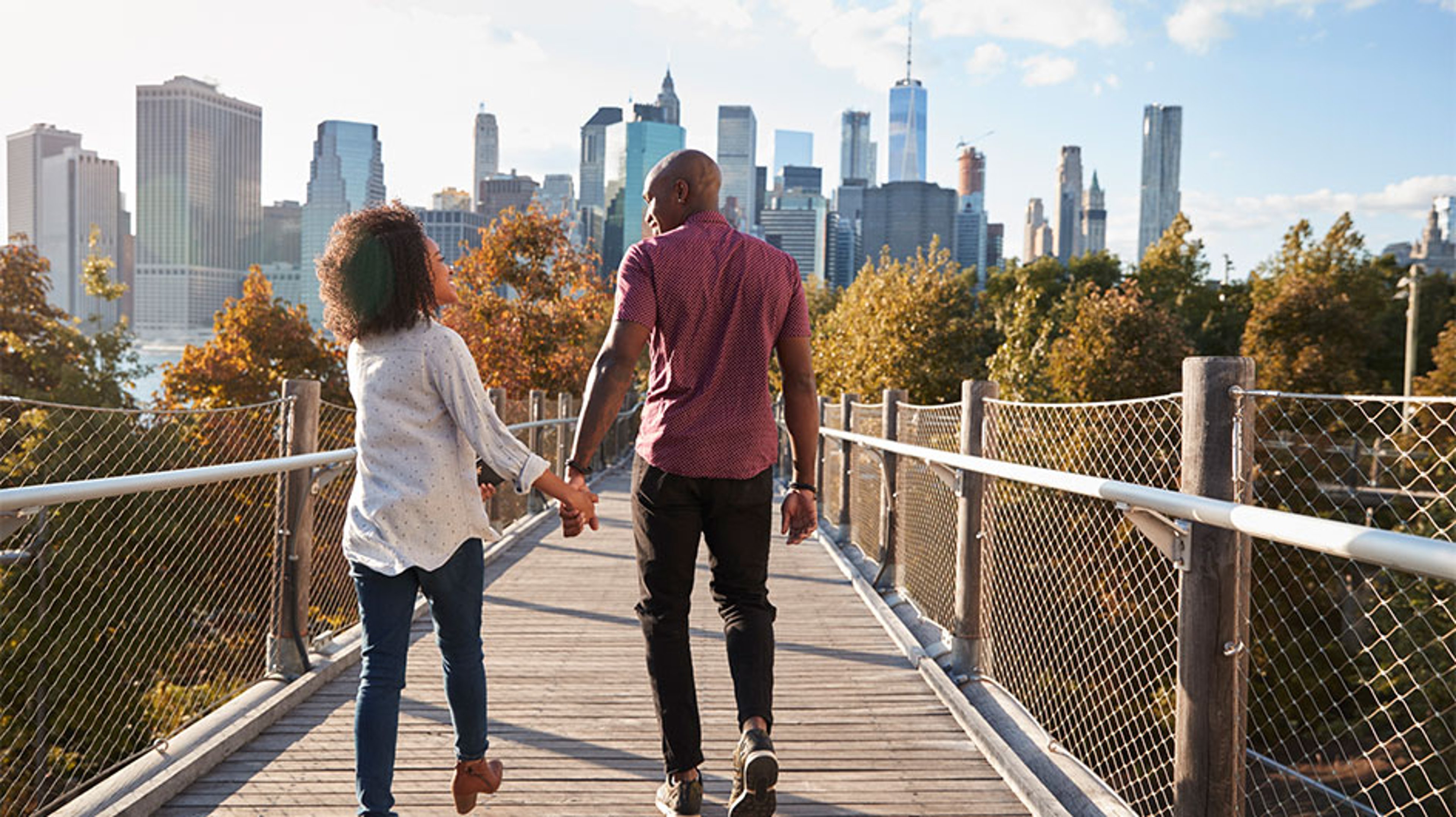 man and woman holding hand walking towards New York City skyline