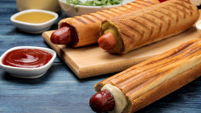 French hot dogs. Tasty hot dogs on the board and sauce on a blue wooden table. fast food street food. sausages in a bun;Credit: Kristina Maksymova
