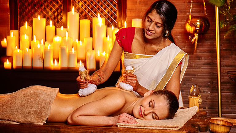 An Ayurvedic therapist performs a traditional herbal poultice massage treatment in India.