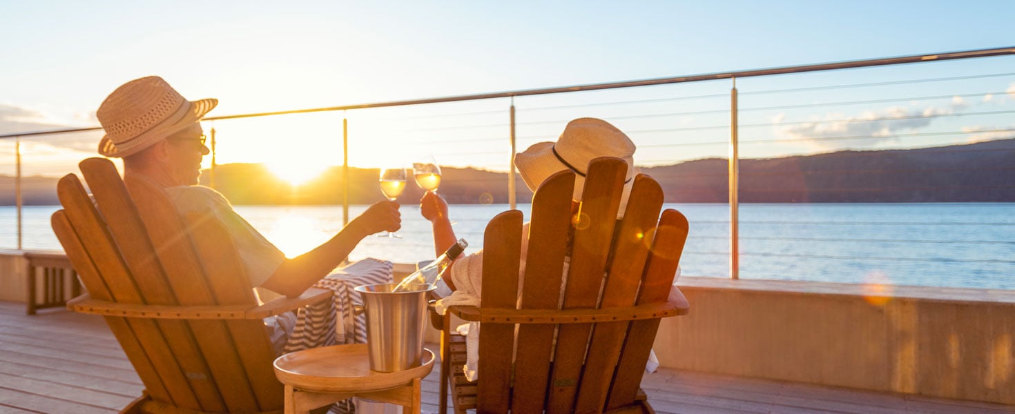 Couple relaxing and drinking wine and toasting on deck chairs in an over water bungalow