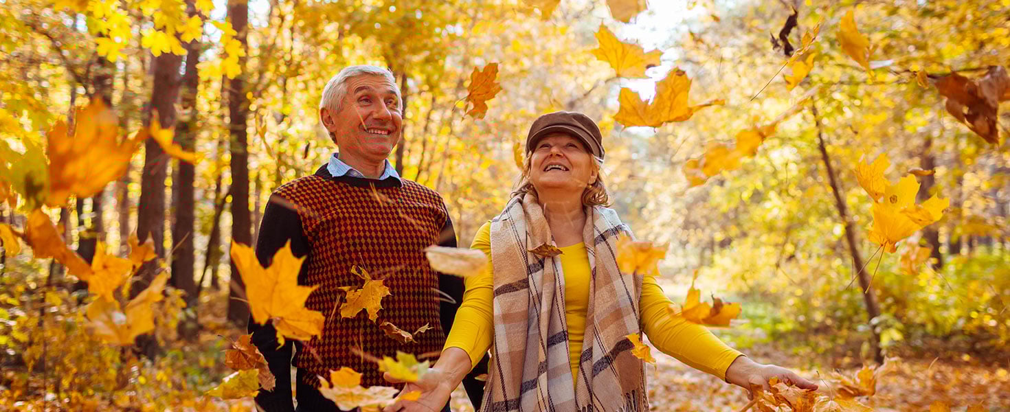 Fall season. Family couple throwing leaves in autumn forest. Senior people having fun outdoors enjoying nature by maryviolet