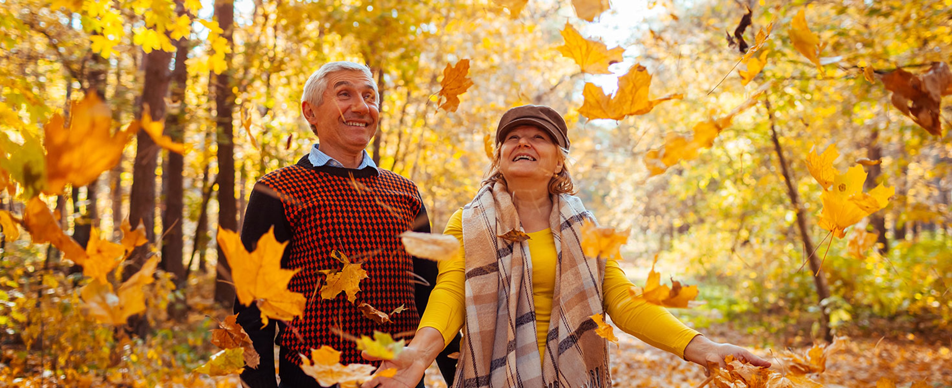 Fall season. Family couple throwing leaves in autumn forest. Senior people having fun outdoors enjoying nature  by maryviolet
