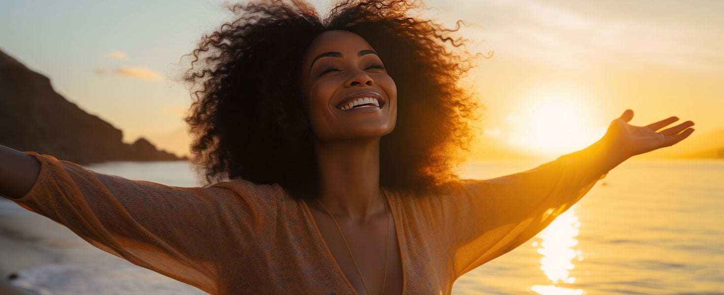 black woman with arms wide open on beach at sunset