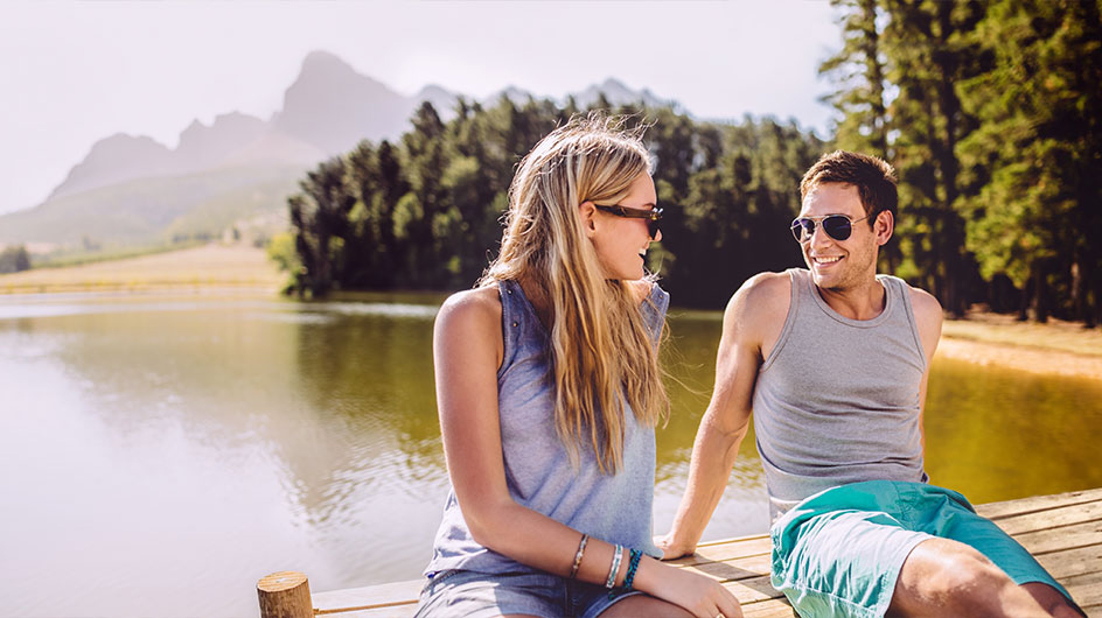 Man and woman sitting on pier wearing sunglasses