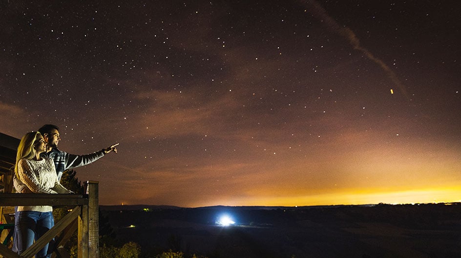man and woman standing on deck, man pointing at night sky