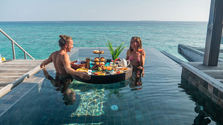 Couple enjoying tropical vacations from an infinity pool in private over water villa. People travel luxury holidays Credit:Mystockimages