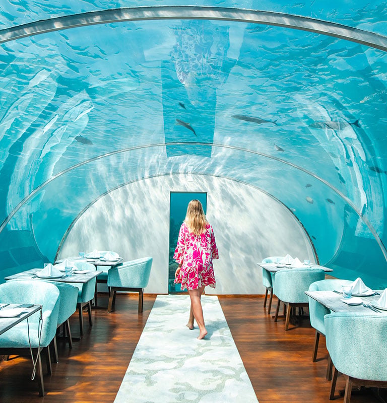 woman walking in elegant fine dining underwater restaurant glass dome in luxury Maldives island resort hotel below water surface Credit:MelanieMaya