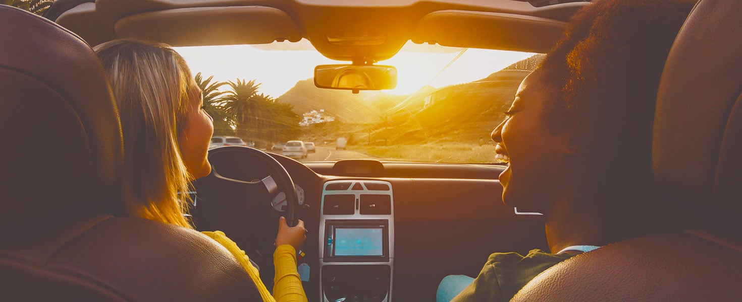 two women inside car driving on road with palm trees