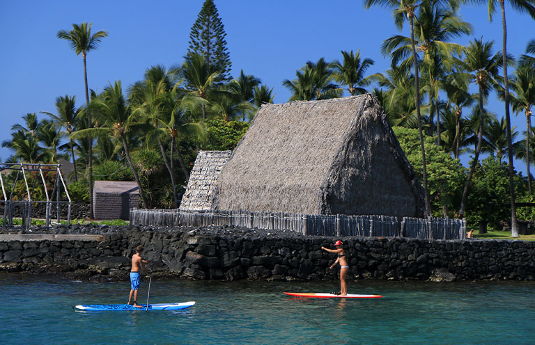 Stand-up Paddle Boarders cross Kamakahonu Bay near Ahuena Heiau, Historic Kailua Village
