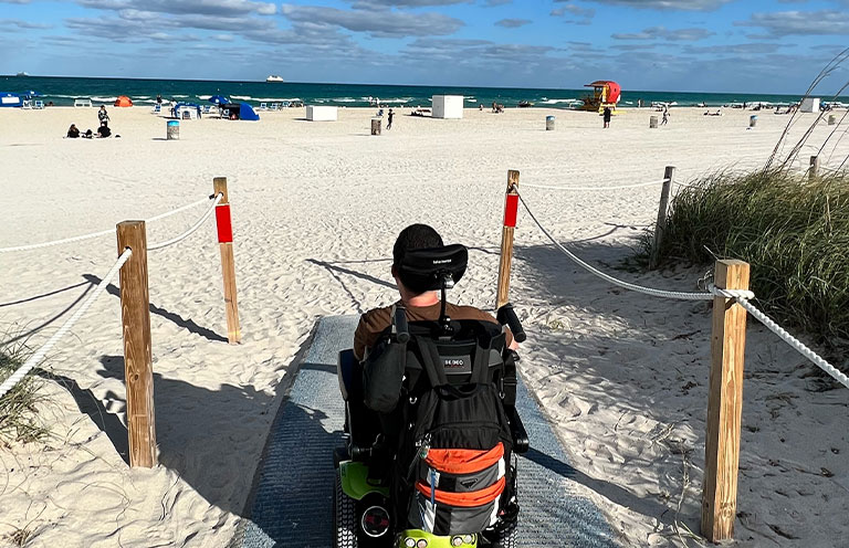 Man in wheelchair on beach mat leading to sand