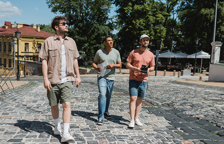 full length of tour guide and multicultural travelers with map and vintage camera walking on pavement of Andrews descent in Kyiv.