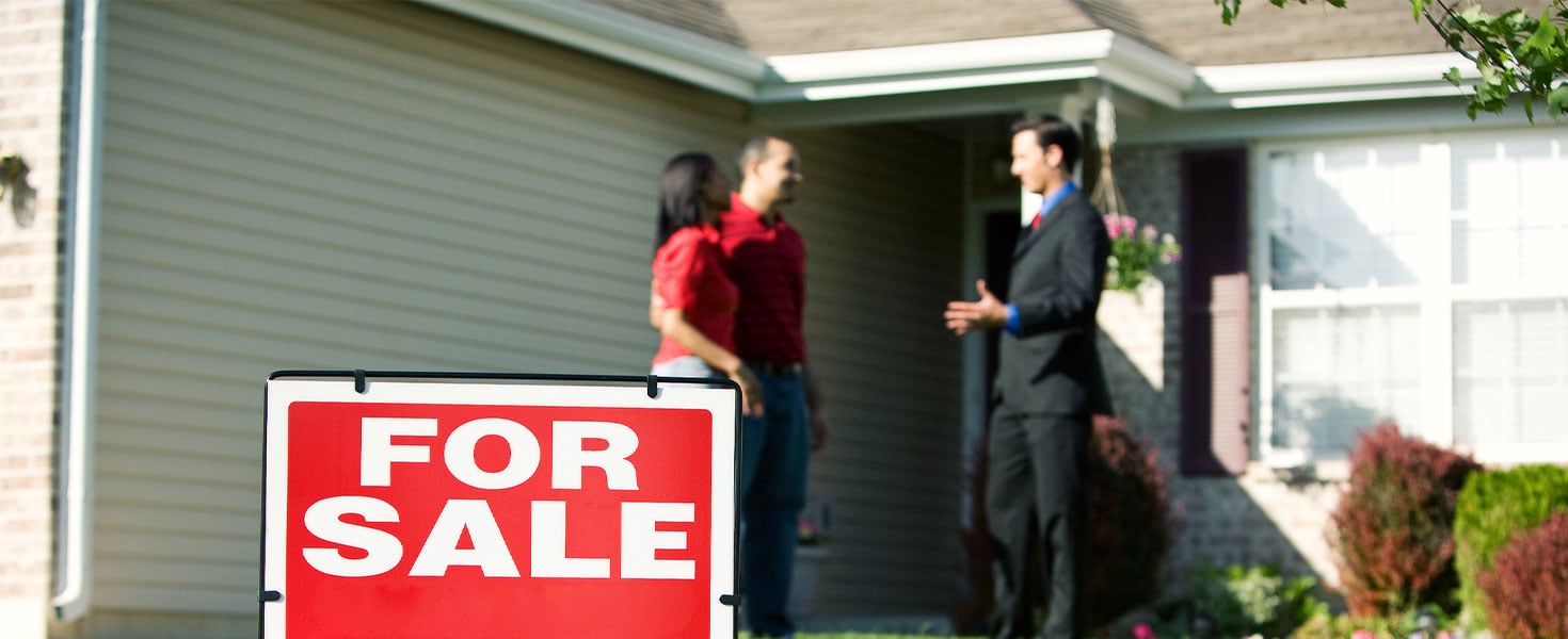 couple talking to real estate agent outside of house with for sale sign