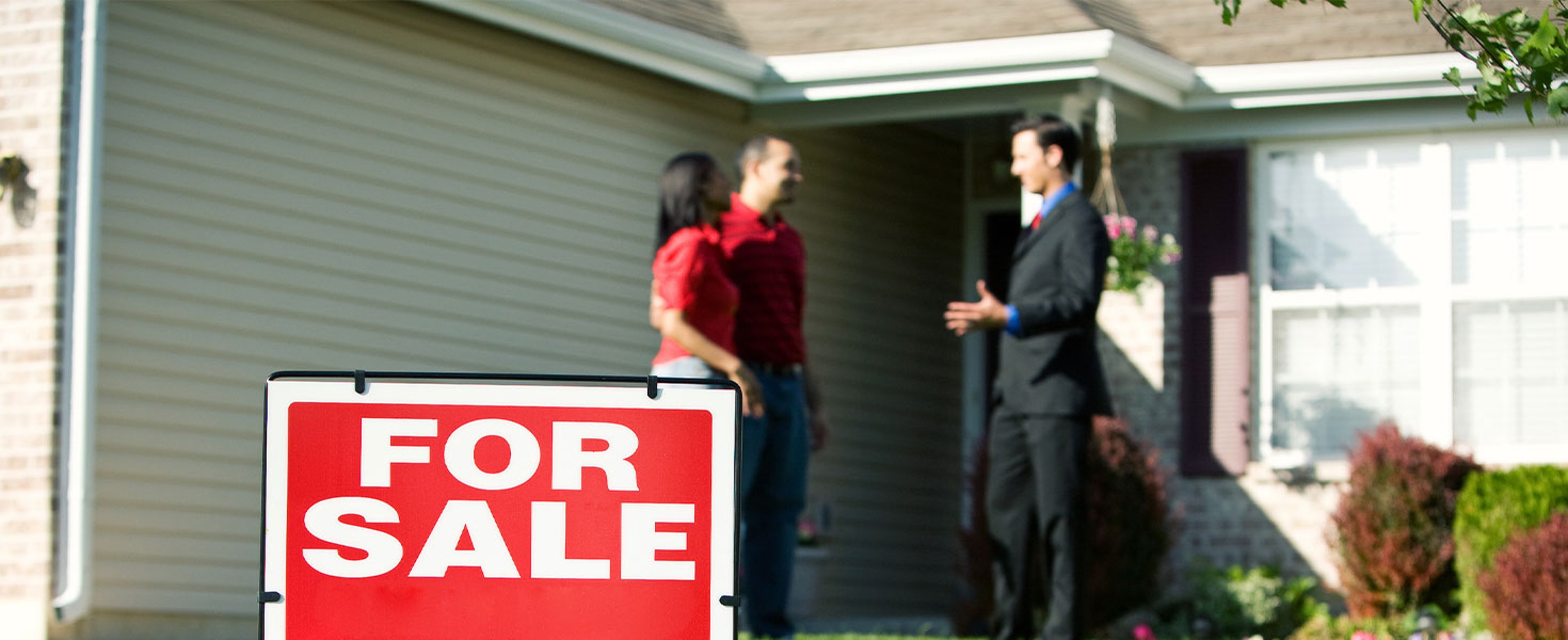 couple talking to real estate agent outside of house with for sale sign