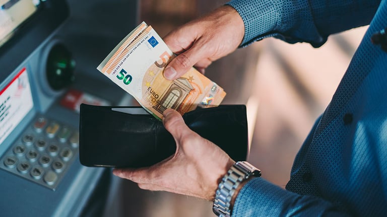 Businessman on business travel withdrawing cash money. Credit: martin-dm
