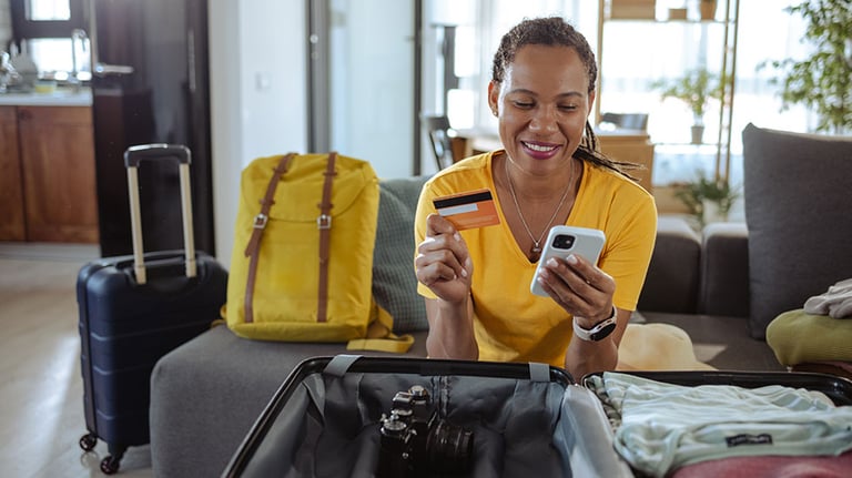 Mature African American woman packing for a trip and using online payment services. Credit: Milko