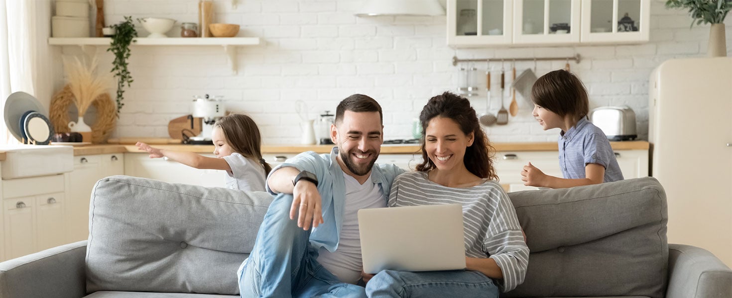 mother and father using laptop while kids play in background