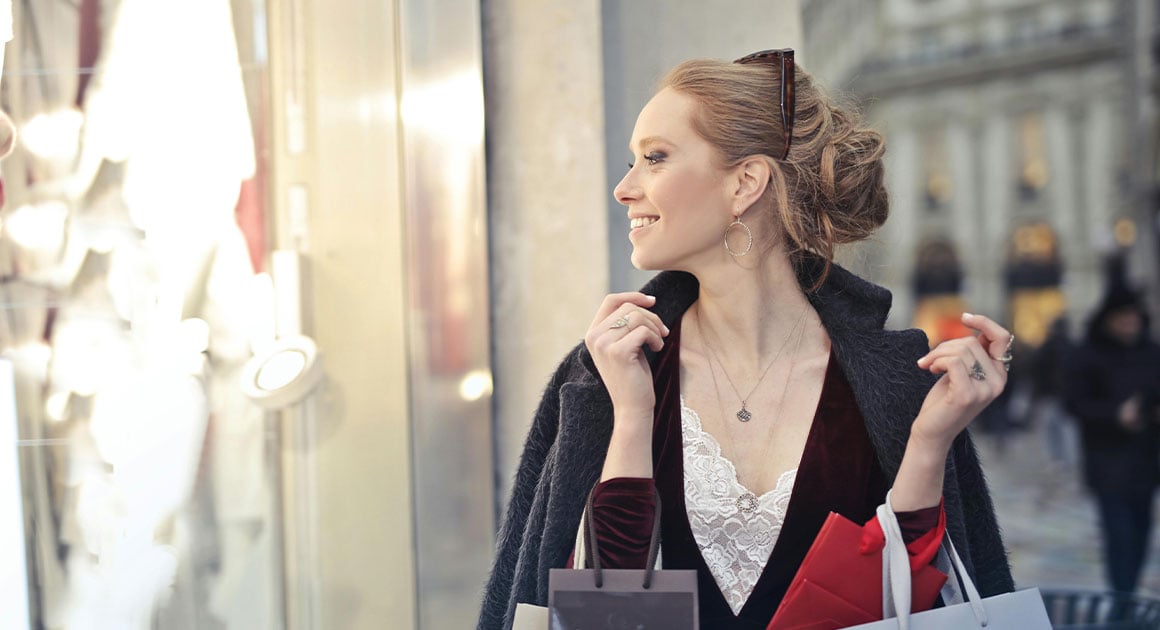 woman holding shopping bags on street looking through store window