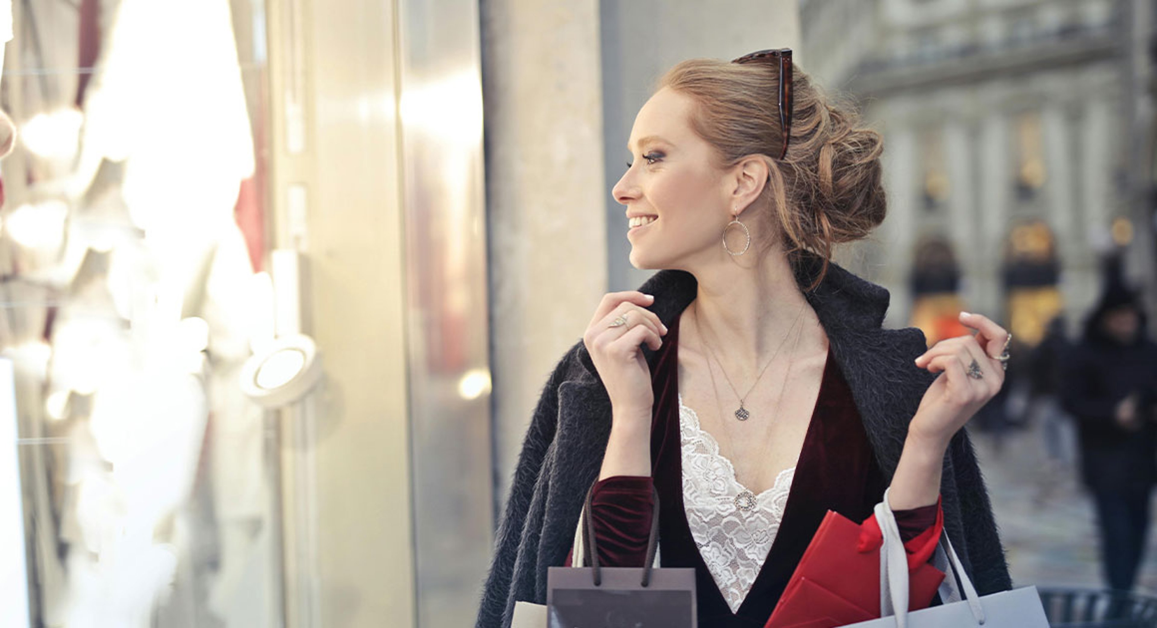 woman holding shopping bags on street looking through store window
