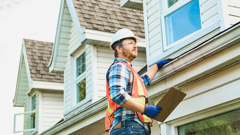 man with hard hat standing on steps inspecting house roof By Louis-Paul Photo