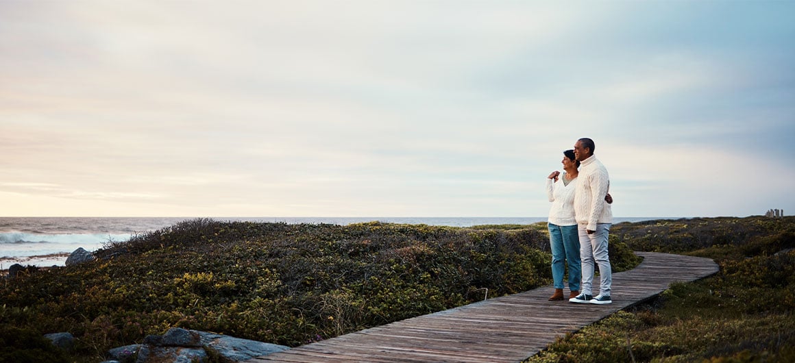 elderly couple hug on a boardwalk at a beach