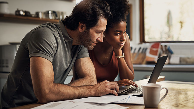 Couple with a laptop doing finance paper work, paying debt insurance loans or online ebanking together at home. Two serious people planning and looking at financial document, bills rate for mortgage  By Allistair/peopleimages.com