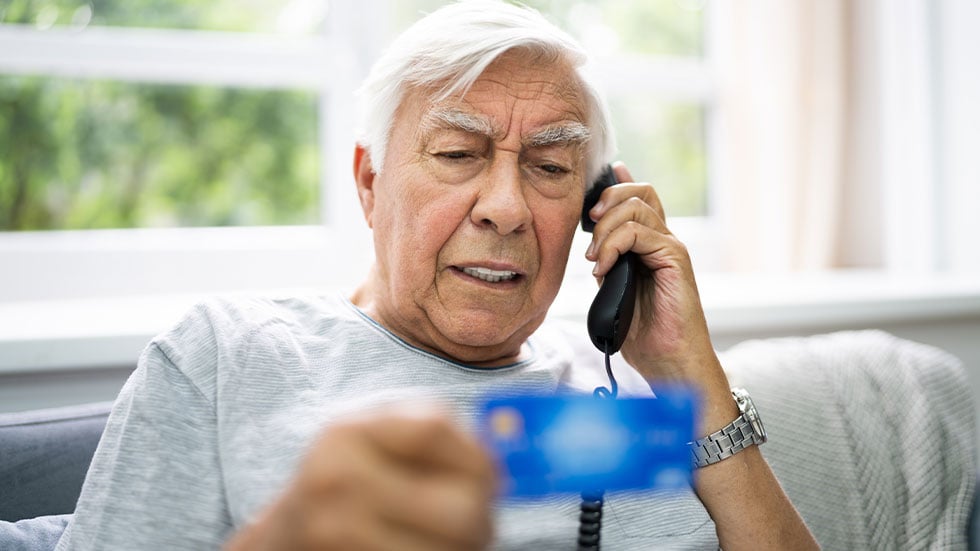 elder man on phone holding a credit card
