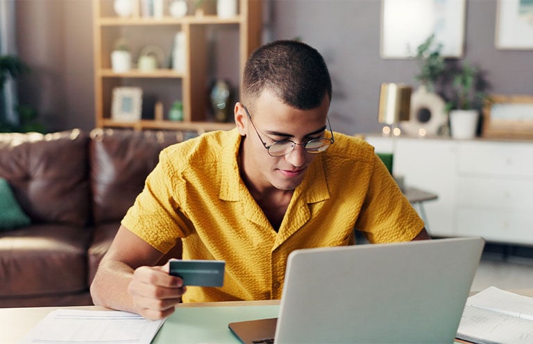 man holding bank card looking at laptop