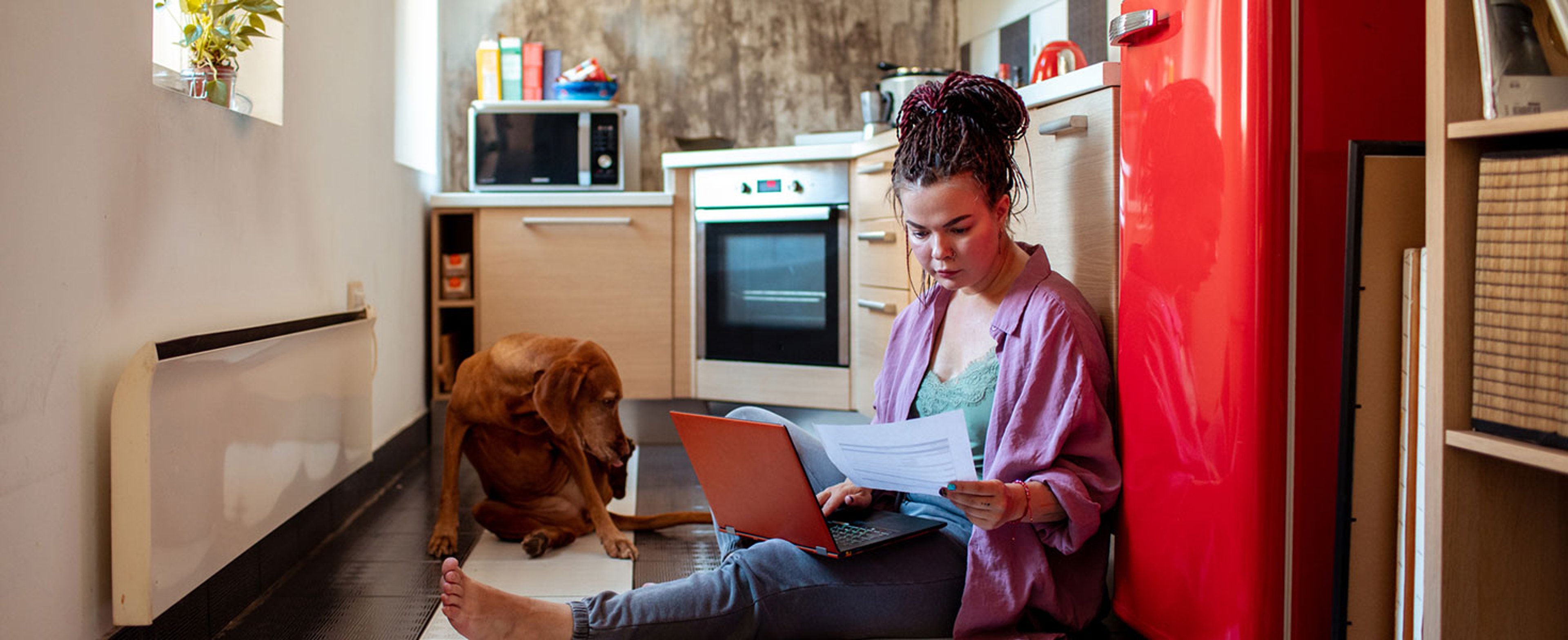 Close up of a young adult woman going over her home finances with her dog next to her Credit:vorDa