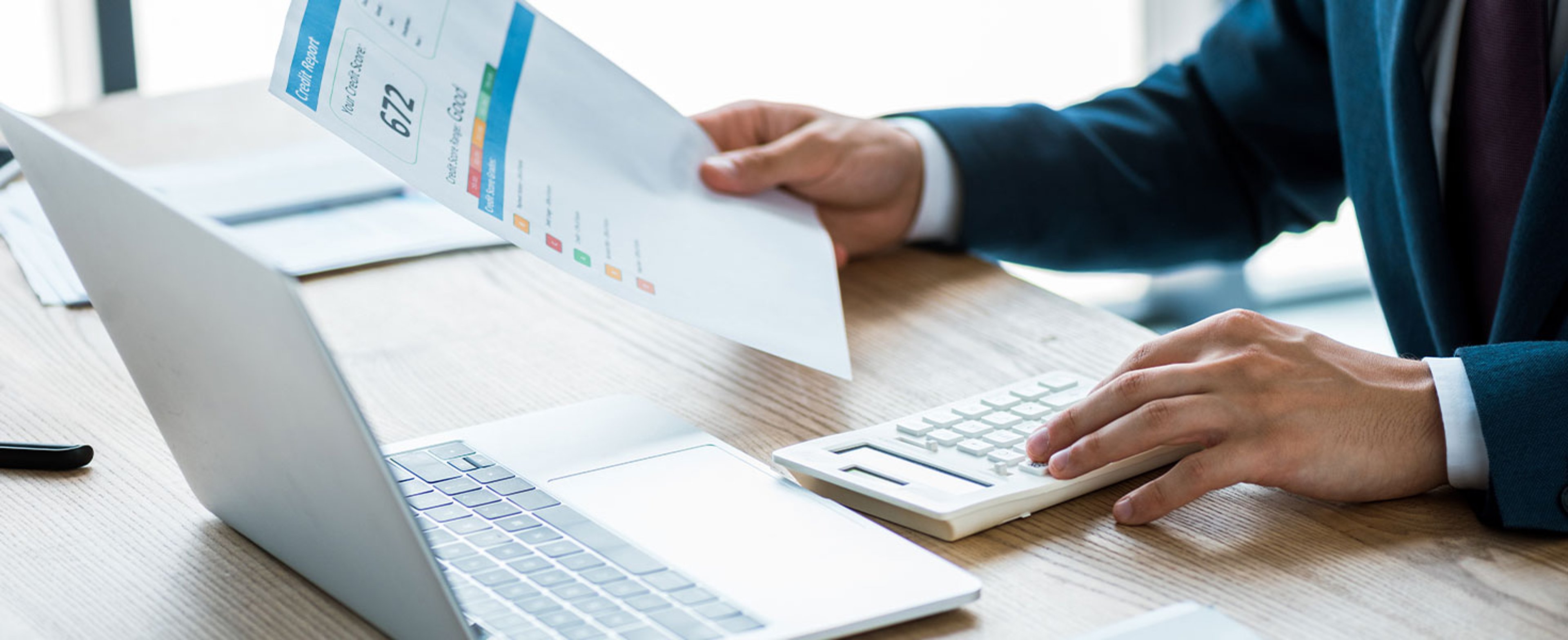 man holding credit report, using calculator, and looking at laptop