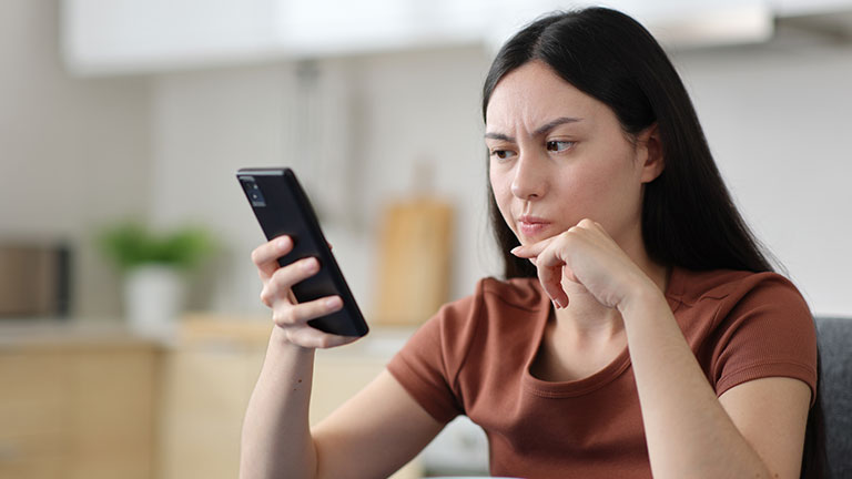 Suspicious asian woman checking phone in the kitchen stock photo; Credit:AntonioGuillem