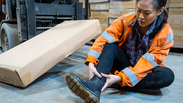 An industrial warehouse workplace safety topic. A female employee injured by tripping over forklift forks. Forks must be placed on the ground to avoid being trip hazards; Credit: Fertnig