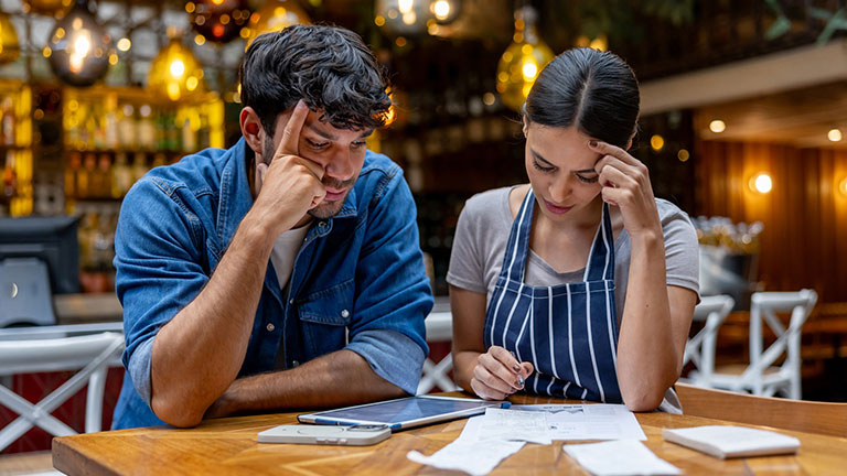 Business owner and waitress doing the accountancy at a restaurant and looking worried - small business concepts; Credit: Hispanolistic