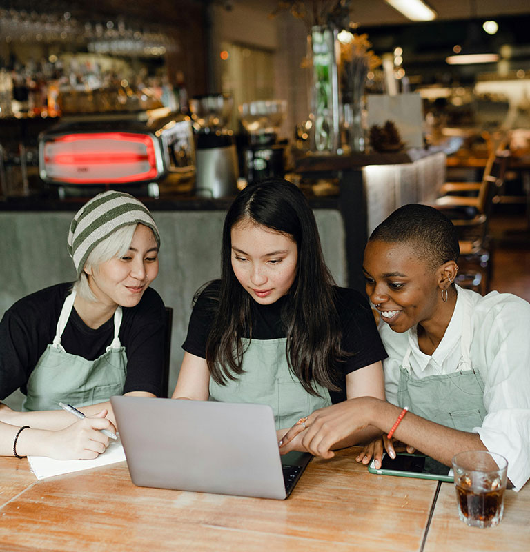 Content colleagues wearing aprons browsing laptop in cafeteria; Credit: Ketut Subiyanto with Pexels