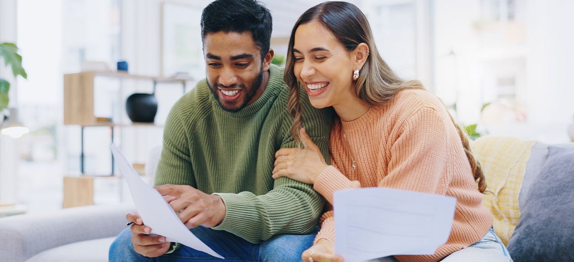 man and woman sitting on couch smiling and looking at papers