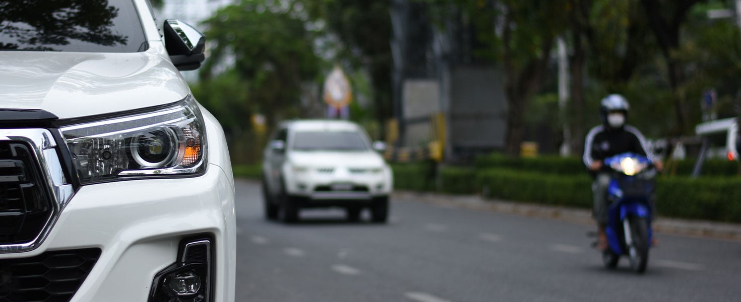 White SUV on road with motorcycle and vehicle behind it