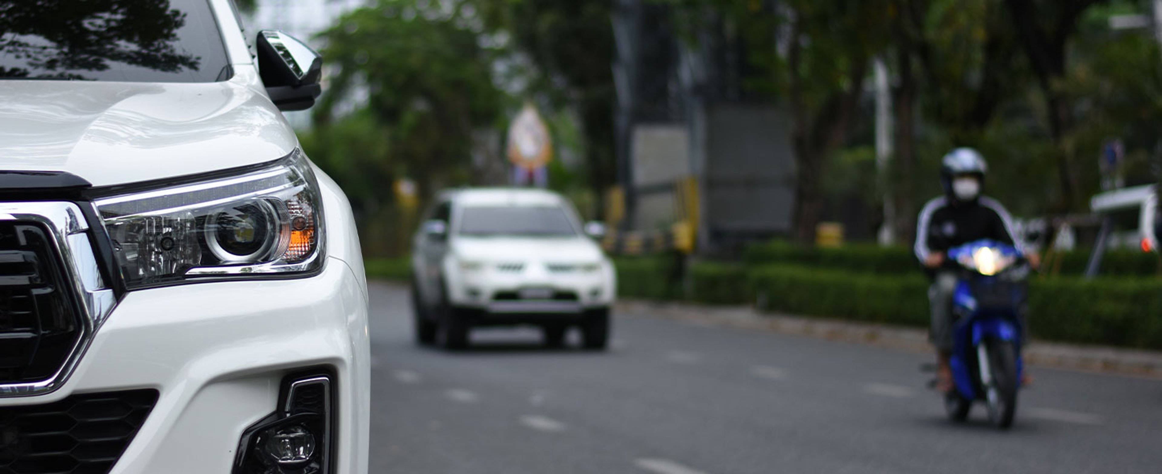 White SUV on road with motorcycle and vehicle behind it